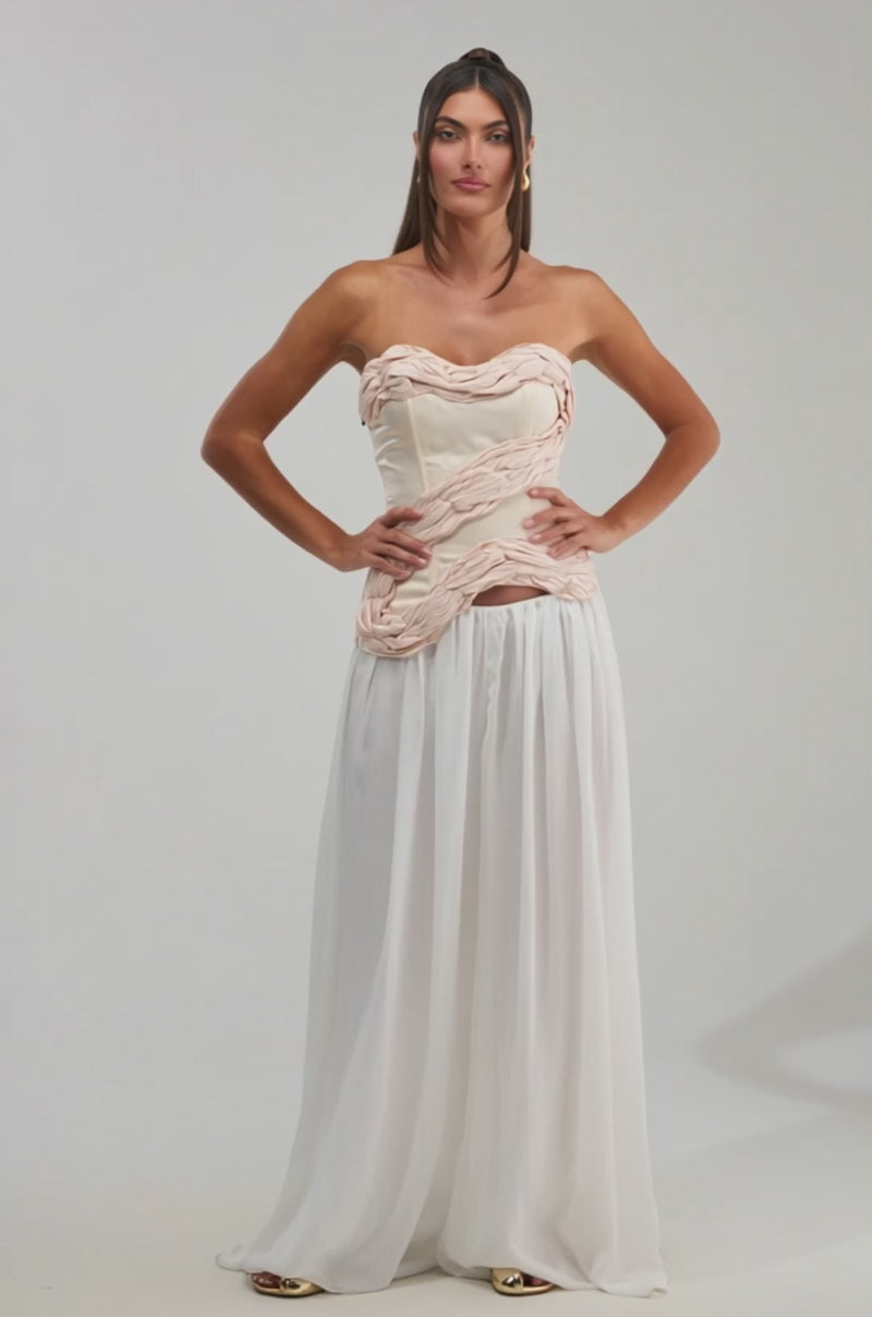 A video of a woman wearing the WHITE HOT SATIN CORSET, a strapless top with a sweetheart neckline and sculpted detailing, styled with a long flowing white skirt. 