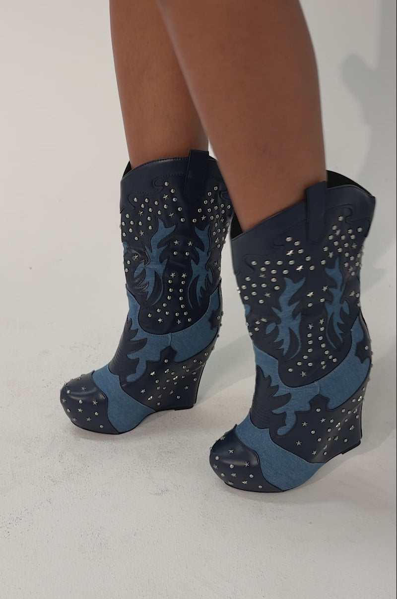 Video of woman modeling the AZALEA WANG CALLIA DENIM WESTERN WEDGE BOOTIE, featuring dark blue denim with star and stud details, standing on a plain light background.