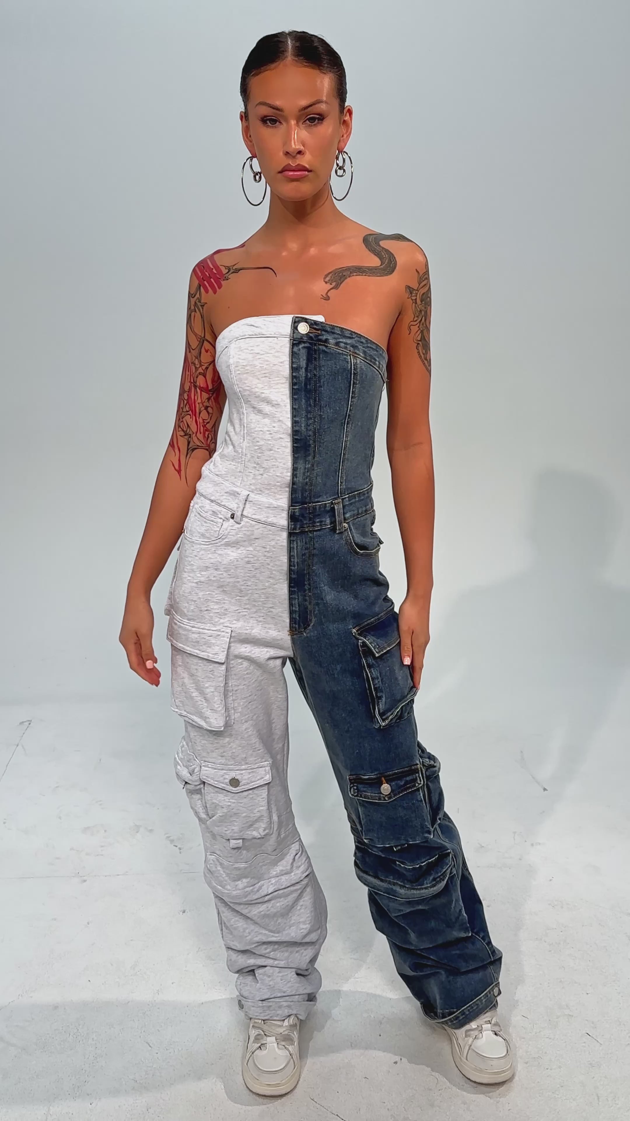 Video of woman modeling the SPLIT DECISION DENIM JUMPSUIT—half light gray, half blue—with a chunky chain necklace and white furry boots, set against a plain light background.