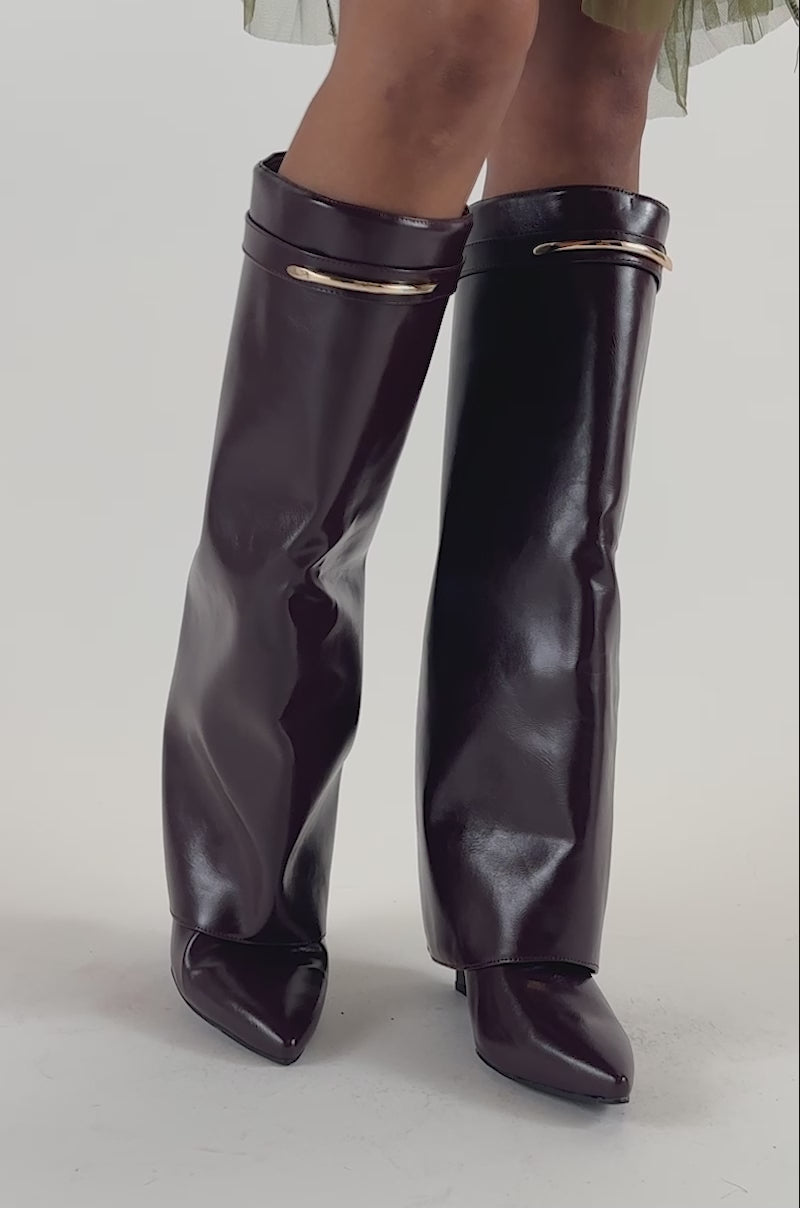 Video of a woman modeling the AZALEA WANG LOVE BURN BURGUNDY SHARK WEDGE BOOT—shiny, knee-high footwear featuring pointed toes and gold accents.