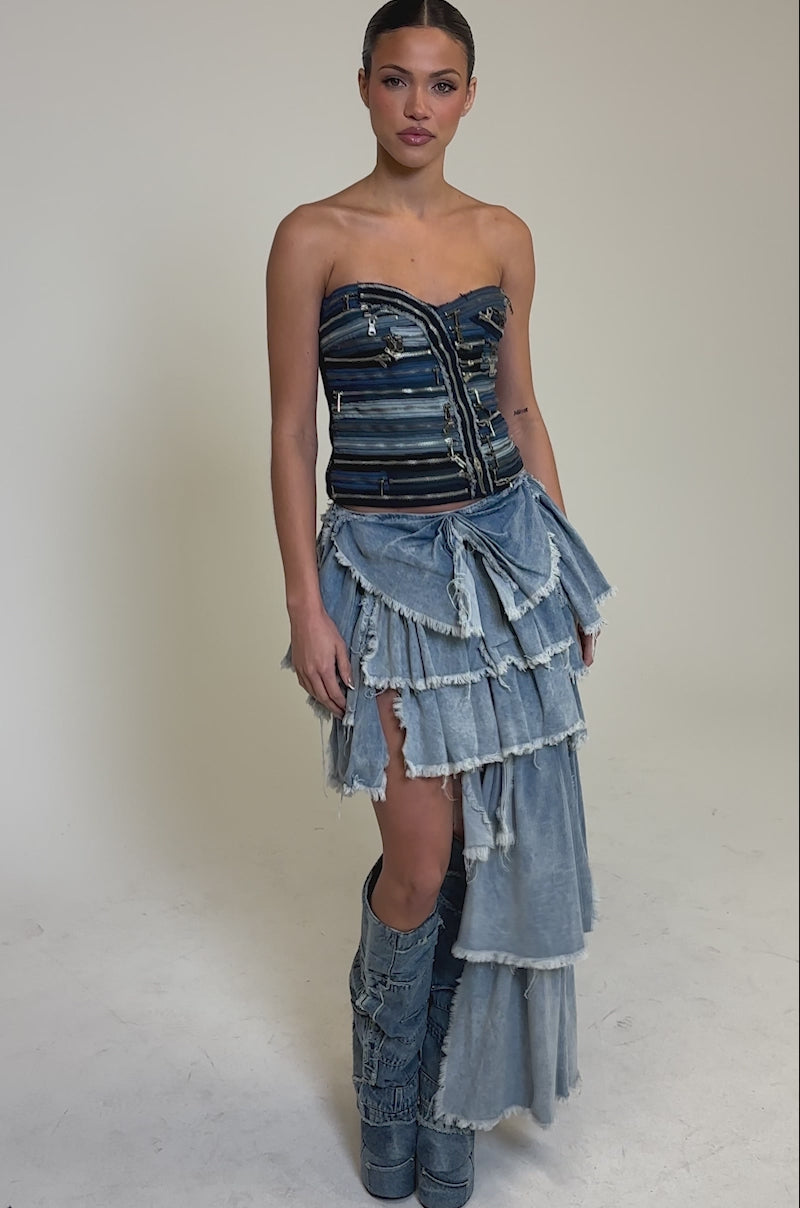 Video of woman modeling the DISTRESSED TIERED ASYMMETRIC MIDI SKIRT and matching high denim boots, standing against a plain background.