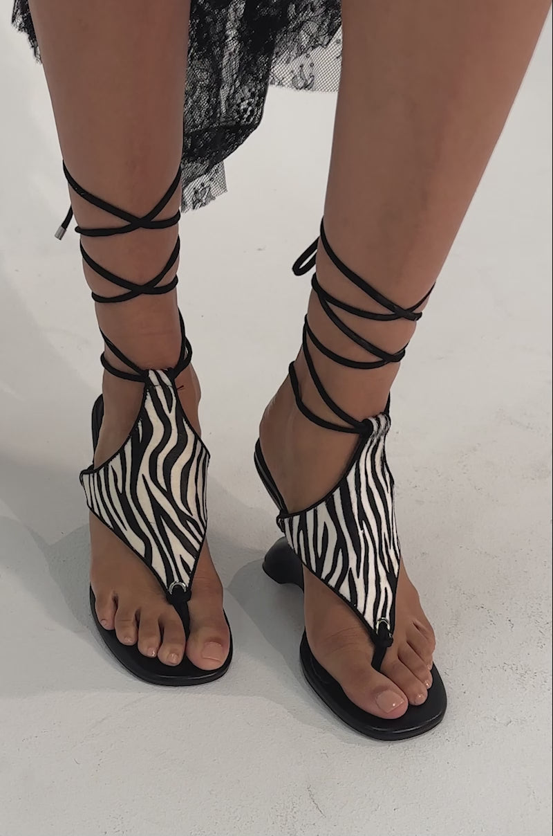 A video of a person wearing AKIRA GOLD JANA BLACK ZEBRA CALF HAIR PRINT WEDGE SANDALS.