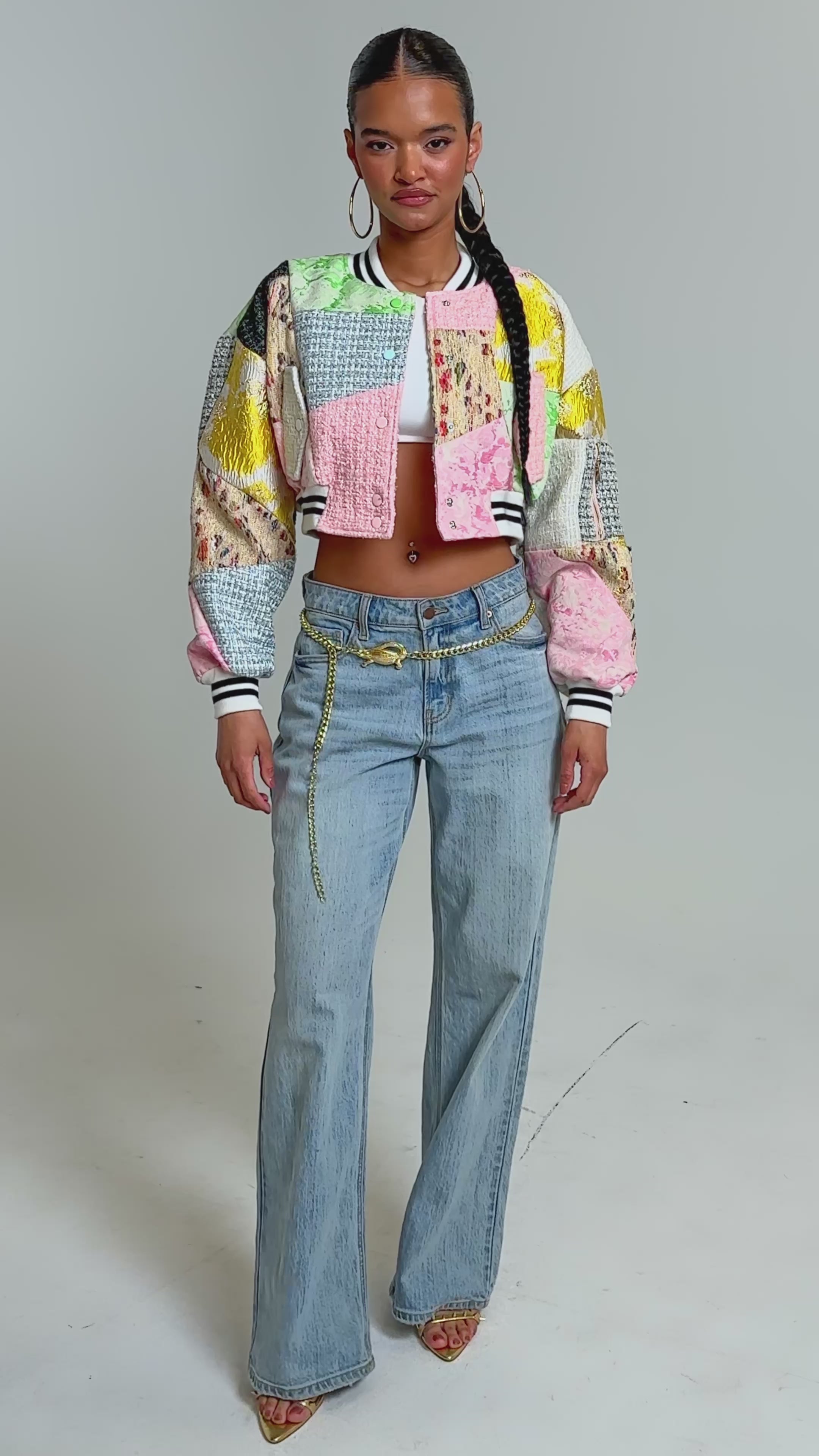 Video of woman modeling the ESTELLE PATCHWORK BOMBER with striped cuffs and light blue jeans featuring a gold chain belt.