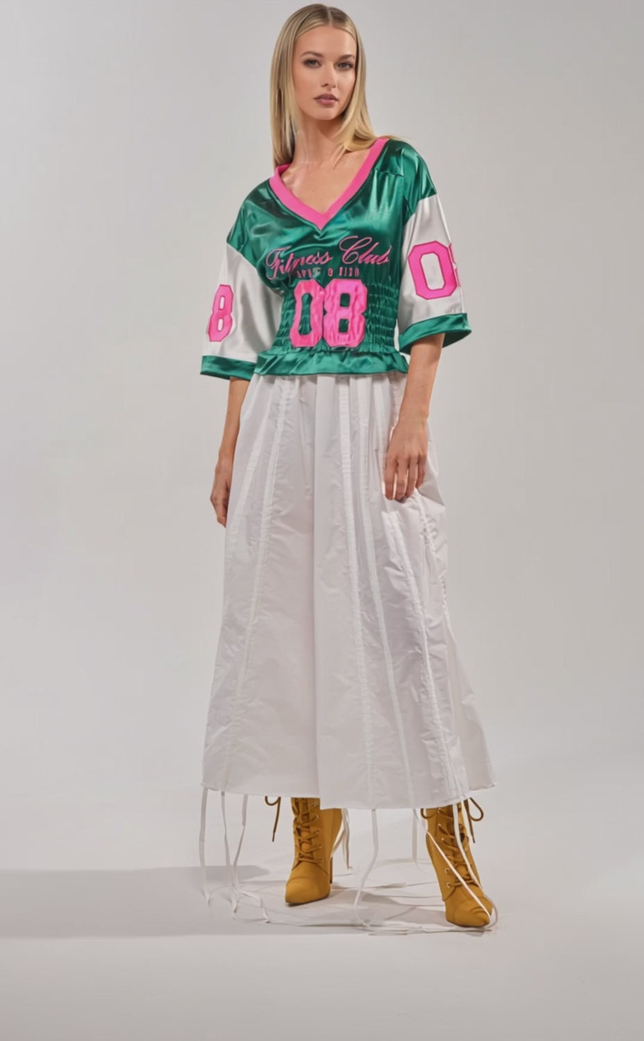 Video of woman modeling the FIX YOUR GAME JERSEY MAXI DRESS, a varsity-inspired green and pink piece with number 08, styled with tan lace-up boots.
