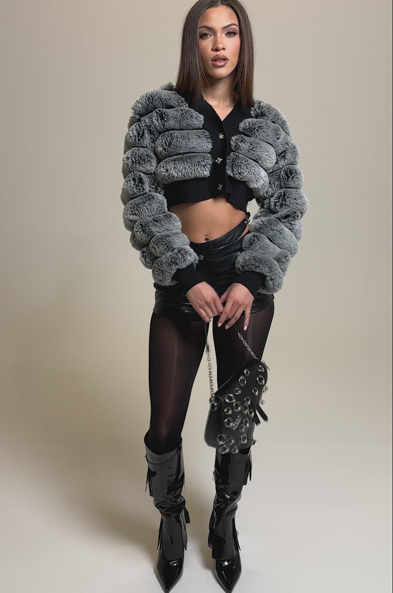 Video of woman modeling the SOMETHING GOOD FAUX LEATHER SHORT with high waist and cutout straps, paired with sheer black tights and a gray fur-textured jacket.