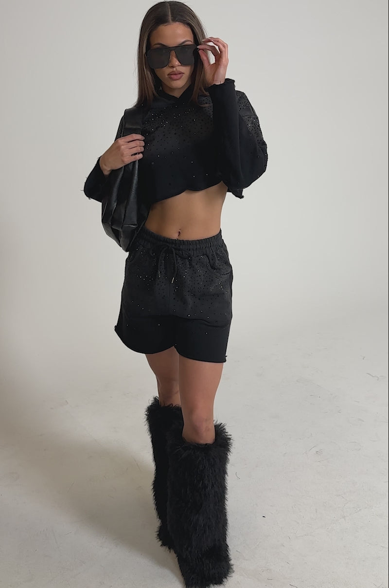 Video of woman modeling the SPARKLE AND SHINE MINERAL WASHED SHORTS, a black cropped hoodie, oversized sunglasses, a large black shoulder bag, and black furry knee-high boots