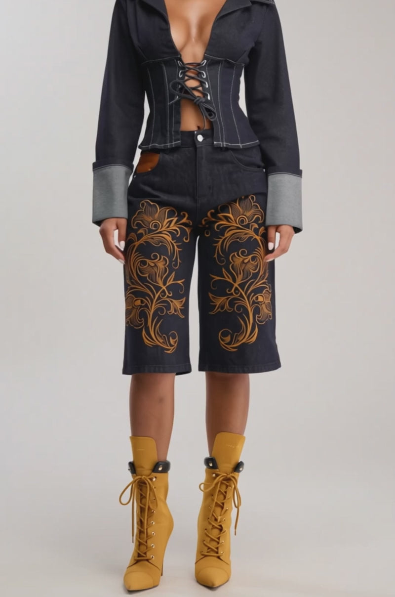 Video of woman modeling the NO BROKE BOYS BERMUDA SHORT in dark wash with orange embroidery, a matching denim jacket with cuffed sleeves, and mustard yellow lace-up heeled boots—ideal for festival streetwear. 