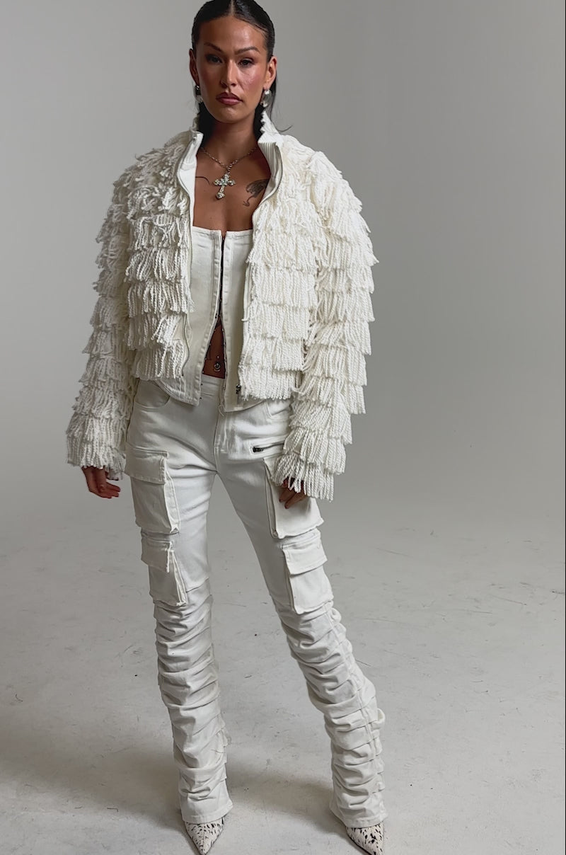 A video of a woman in the FREYA FRINGE BOMBER, paired with a white strapless top and ruched white cargo pants. 