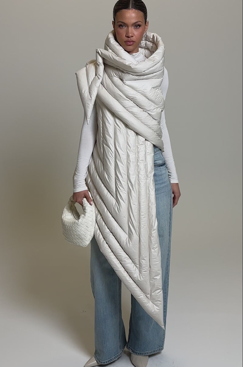 Video of woman modeling the FOR THE DRAMA PUFFER VEST IN IVORY over a fitted white top and wide-leg light blue jeans, accessorized with a textured white clutch and pointed-toe shoes, posed against a plain background.