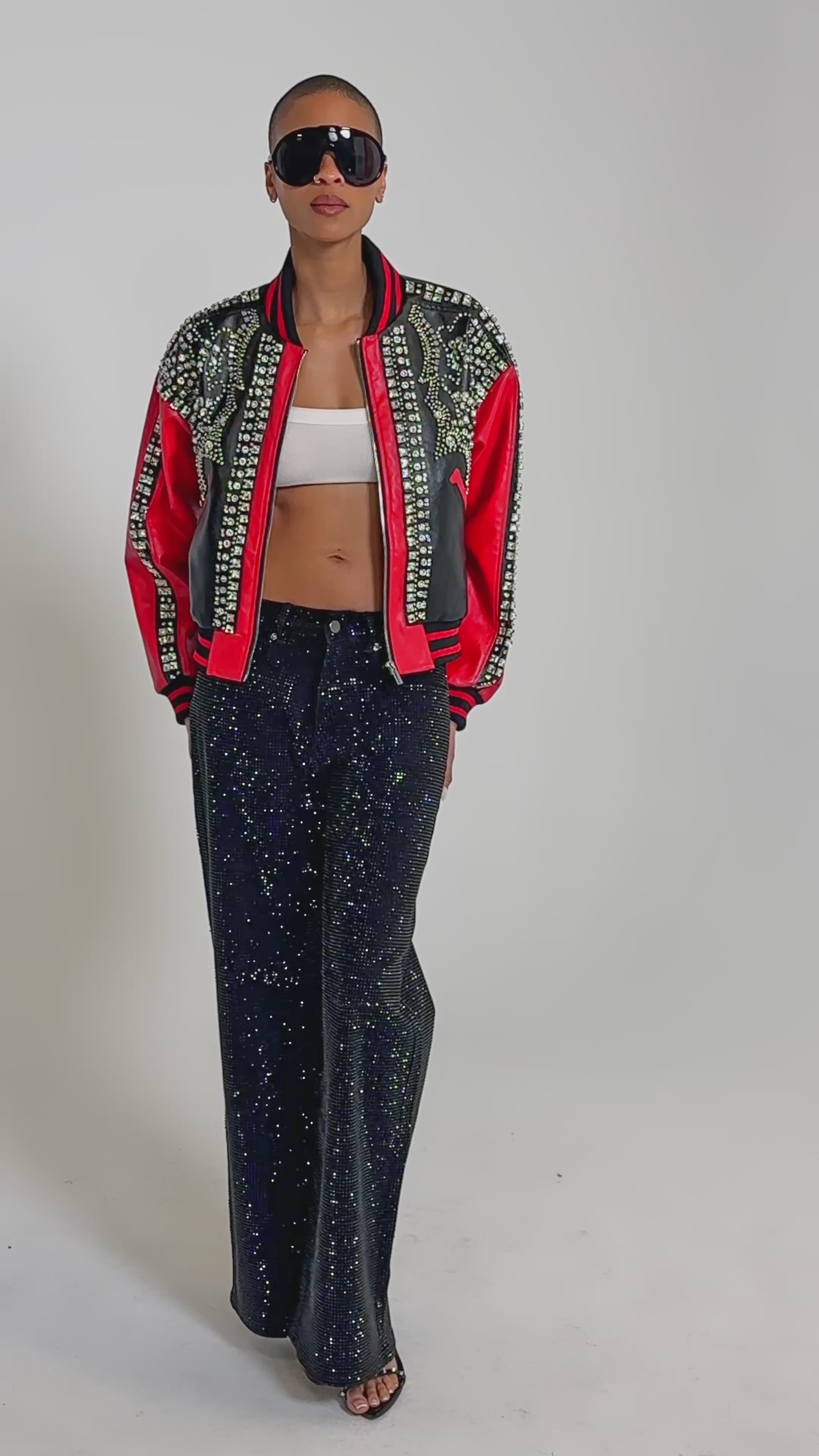 Video of woman modeling the STOLE THE SHOW EMBELLISHED BOMBER, large black sunglasses, a white crop top, and black pants.