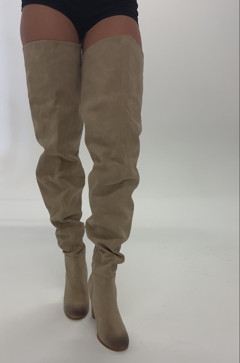 Video of woman modeling the AZALEA WANG NANETTE TAUPE SLOUCHY BOOT, featuring tan faux suede, chunky high heels, and side zippers, while standing against a plain light background.