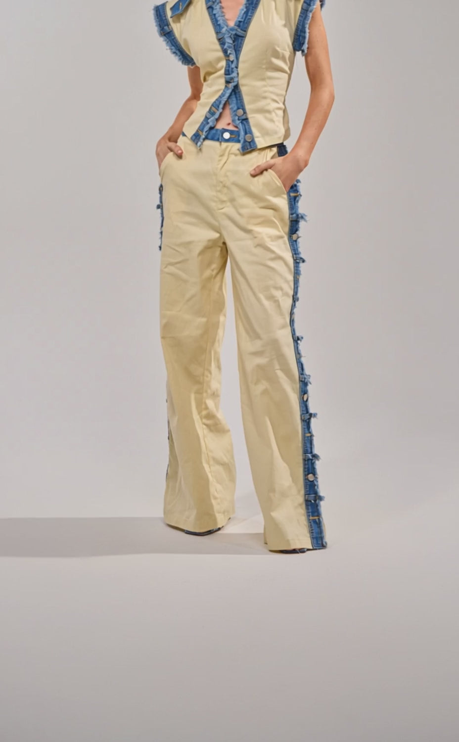 Video of woman modeling the DO YOU LOVE ME TROUSER, which are high-waisted beige linen pants featuring a wide-leg silhouette and frayed blue denim trim on the sides. 