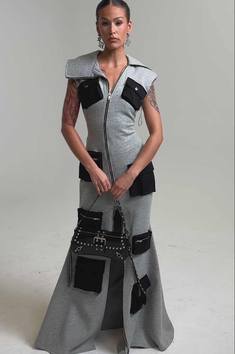 Video of woman modeling the DON'T MESS WITH ME Collared Maxi Dress in grey scuba, featuring a zip front and multiple black pockets, while holding a black studded bag against a light background.
