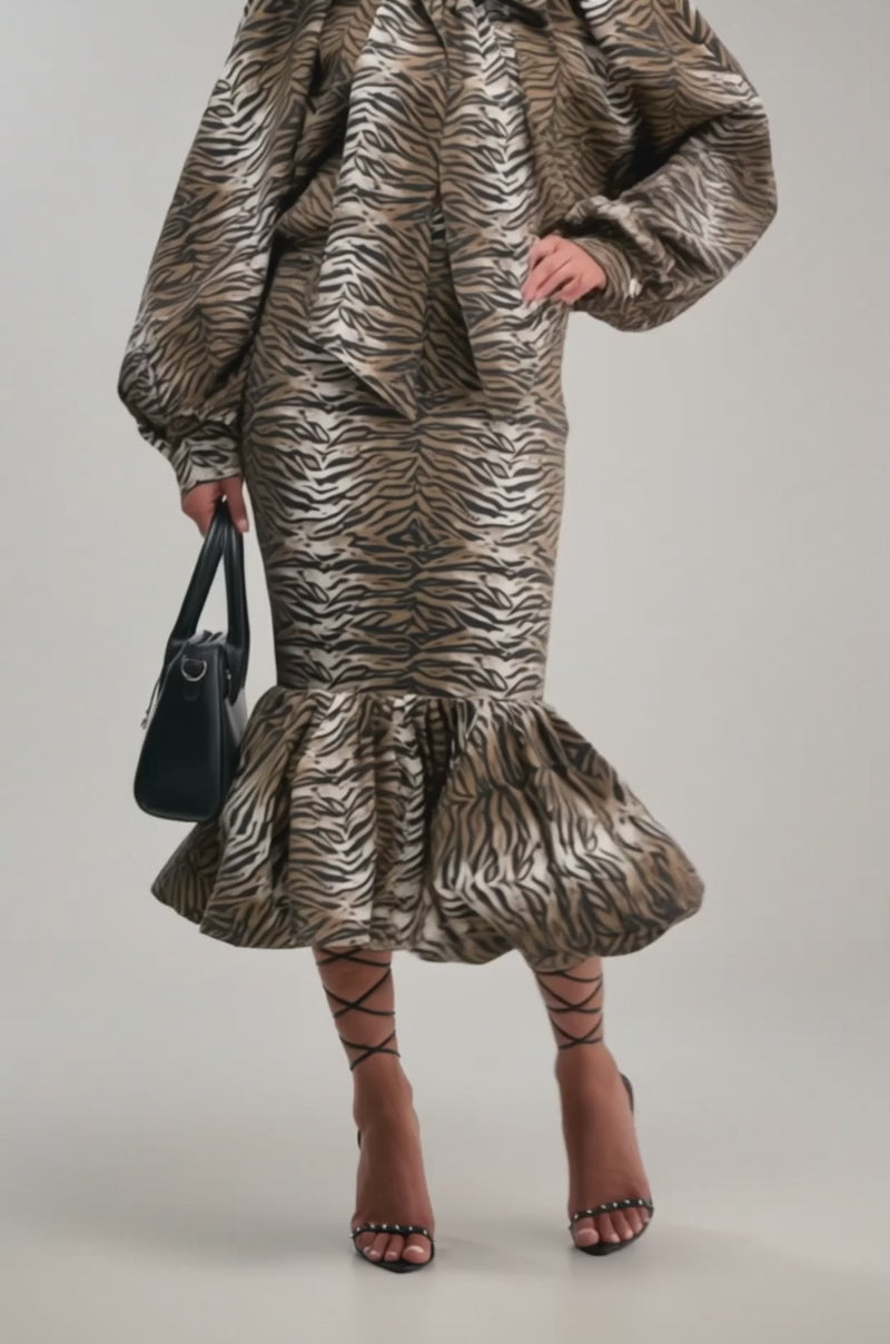A video of a person wearing the INTO THE WILD ZEBRA MIDI SKIRT with a matching puff-sleeve top, black strappy high-heeled sandals, and a black handbag.