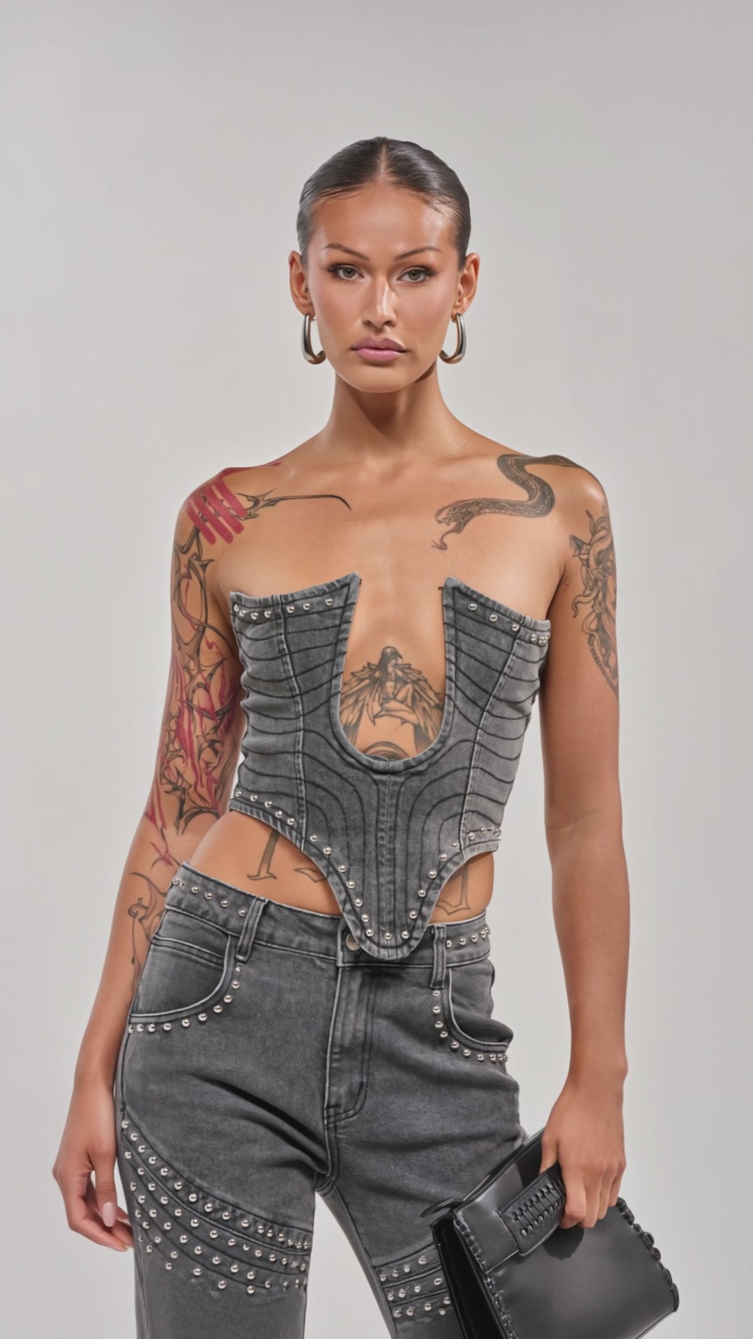 Video of woman modeling the FEELING THE VIBES DENIM CORSET and matching studded jeans, showing off visible tattoos on their arm and chest for an edgy concert-ready look.