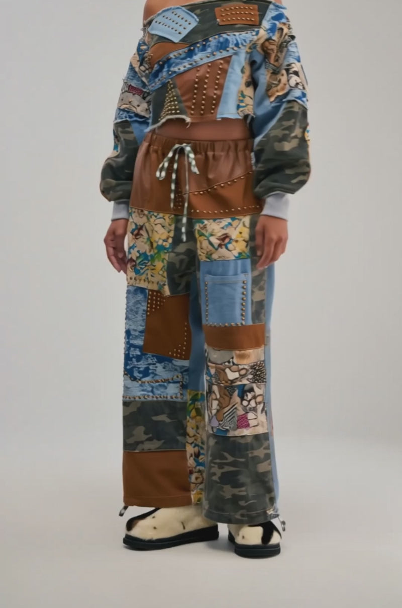Video of a woman modeling the CALL ME CRAZY Patchwork Off the Shoulder Sweatshirt in Brown Multi—an edgy, streetwear-inspired piece featuring denim, brown fabric, and camouflage patches with metal studs and embroidered details.