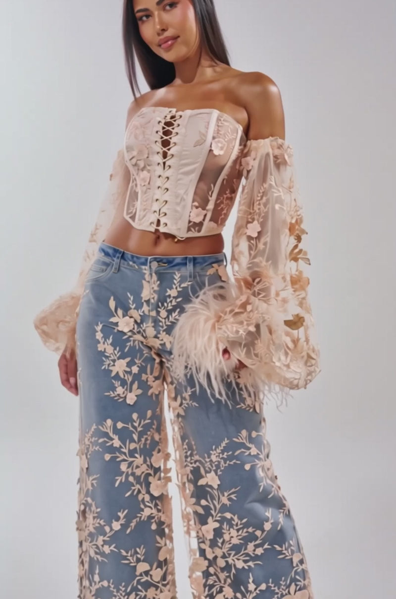 Video of woman modeling the FLY AWAY WITH ME FLORAL CORSET, featuring cream mesh, off-the-shoulder sleeves, and sheer floral embroidery, paired with embroidered blue jeans 