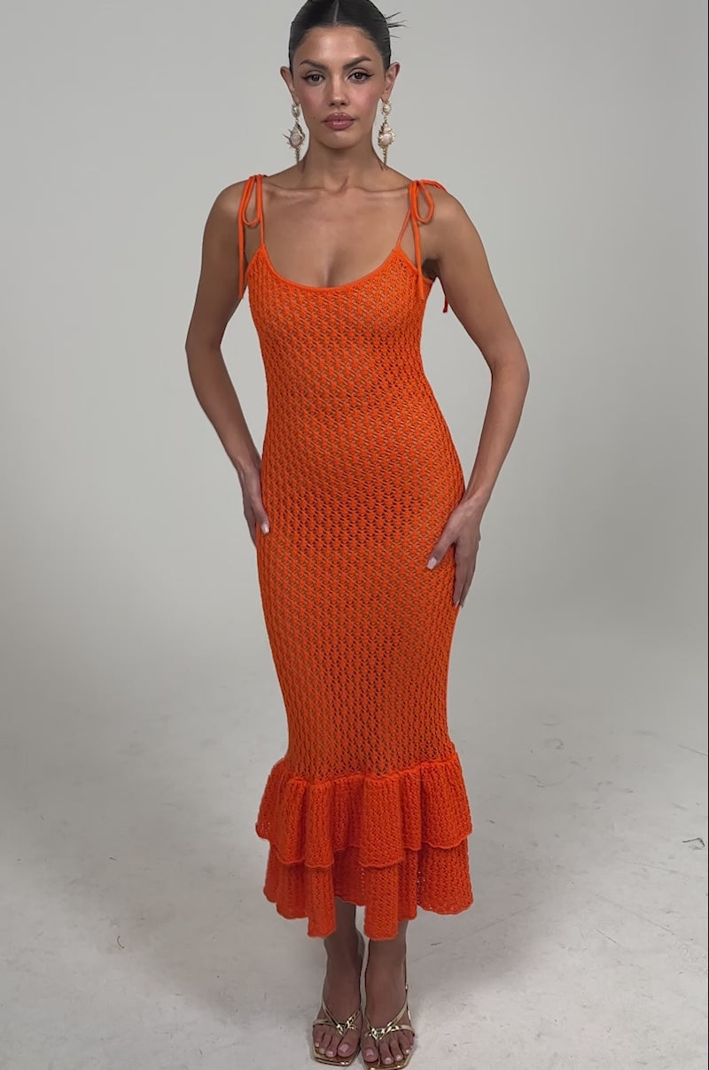 Video of woman modeling the LINSEY MAXI KNIT DRESS IN ORANGE, featuring a ruffled hem and spaghetti straps. She completes her look with gold earrings and strappy heels.