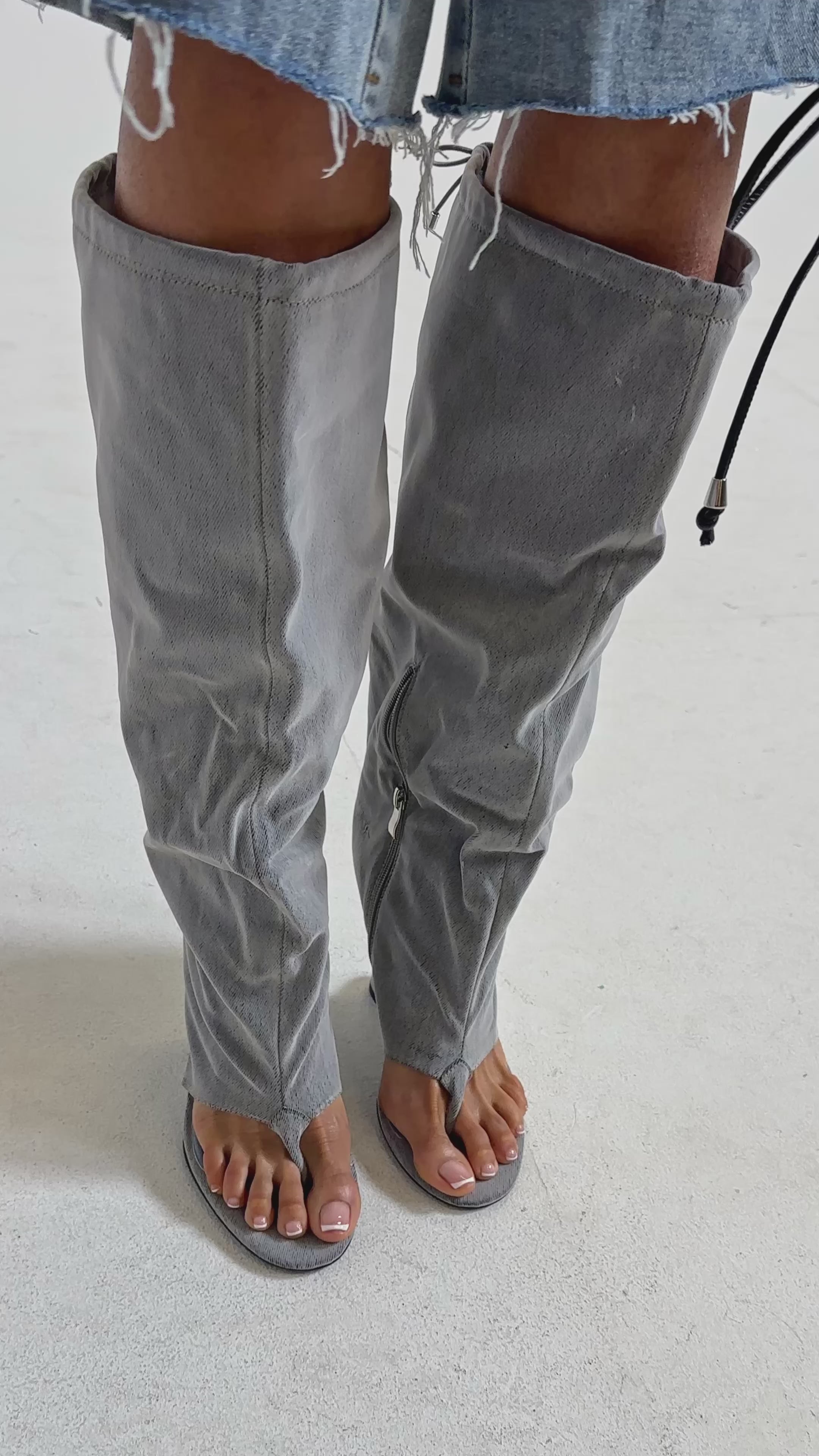 Video of woman modeling the AZALEA WANG XYLAH GREY WEDGE GLADIATOR SANDAL—unique gray knee-high sandals with a loose, slouchy fit, open toes and heels, zippers, and drawstrings—standing against a plain light background.