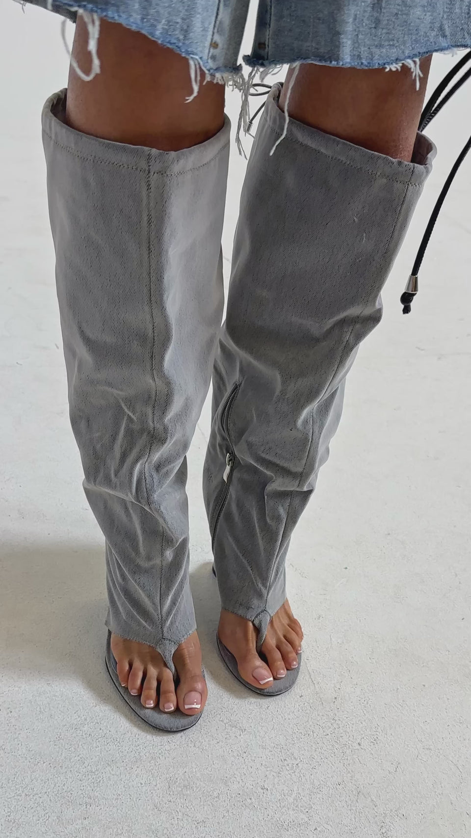 Video of woman modeling the AZALEA WANG XYLAH GREY WEDGE GLADIATOR SANDAL—unique gray knee-high sandals with a loose, slouchy fit, open toes and heels, zippers, and drawstrings—standing against a plain light background.