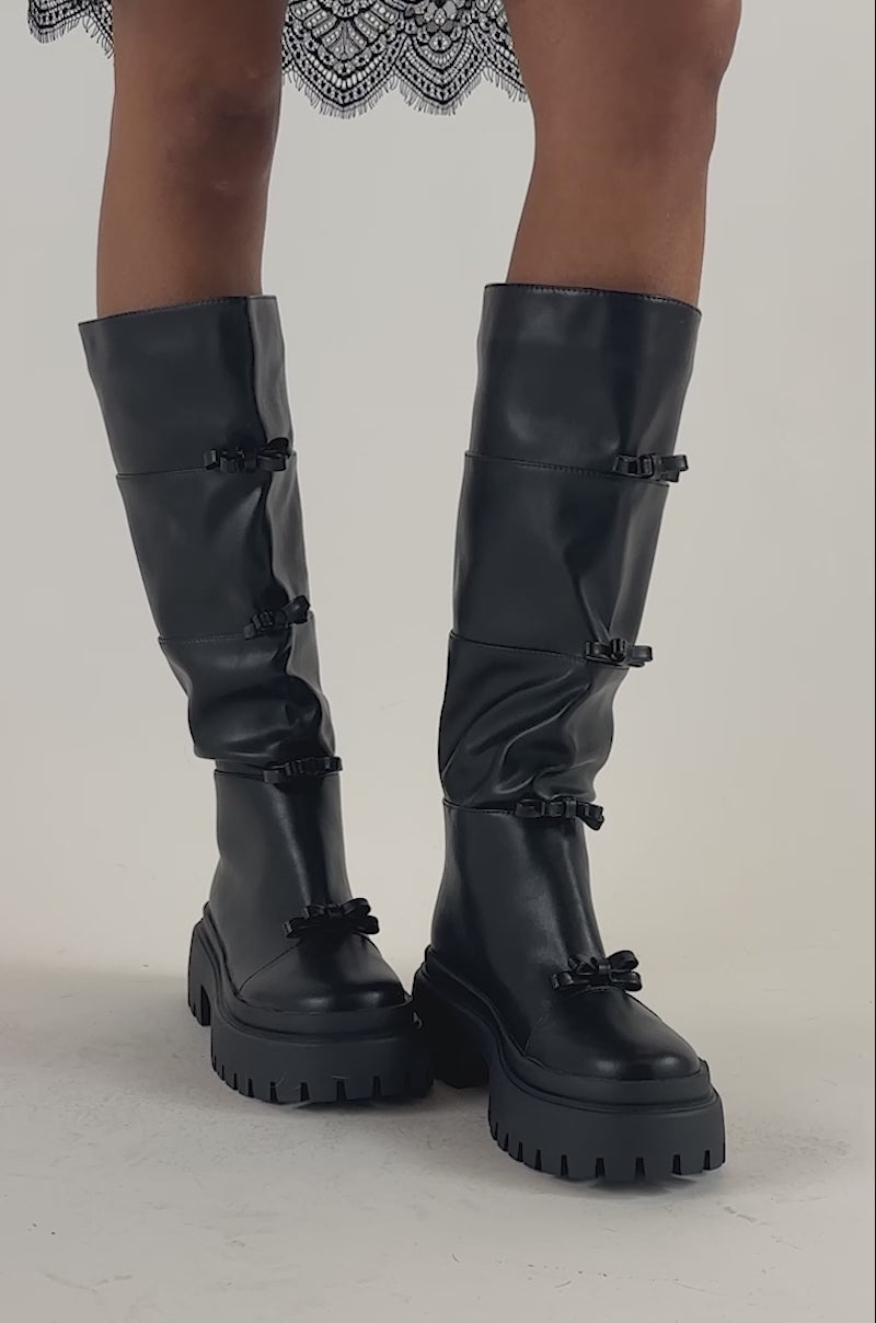 Video of a woman modeling the AZALEA WANG MARGUERITE BLACK PU COMBAT BOOT with chunky soles and decorative bows.