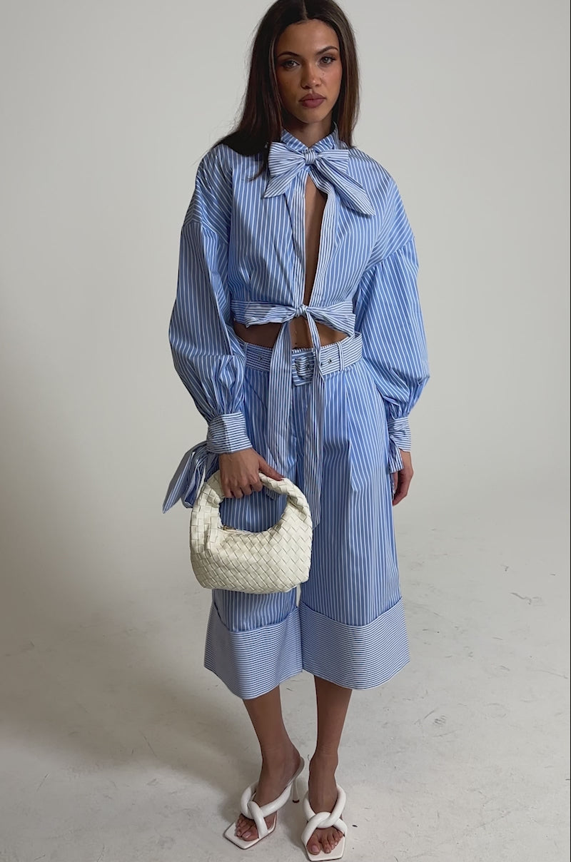Video of woman modeling the NOT LIKE ANYONE ELSE POPLIN SHORT with a blue-and-white pinstripe pattern, styled with a matching blouse, white sandals, and holding a small white woven handbag.