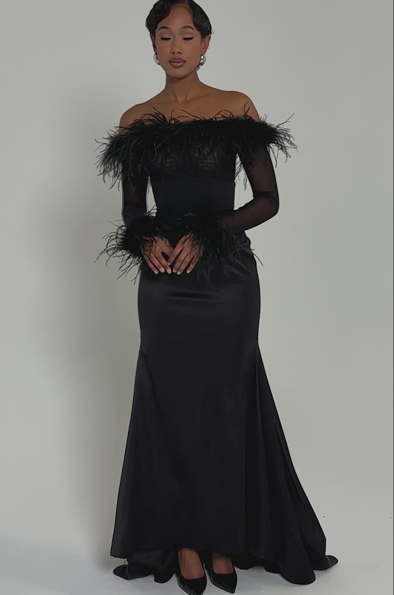 Video of woman modeling the LUXURY LIFE MAXI SKIRT, a long black skirt with feather details and a corset waistband. Its fitted bodice and flowing silhouette evoke timeless elegance against a plain, light background.