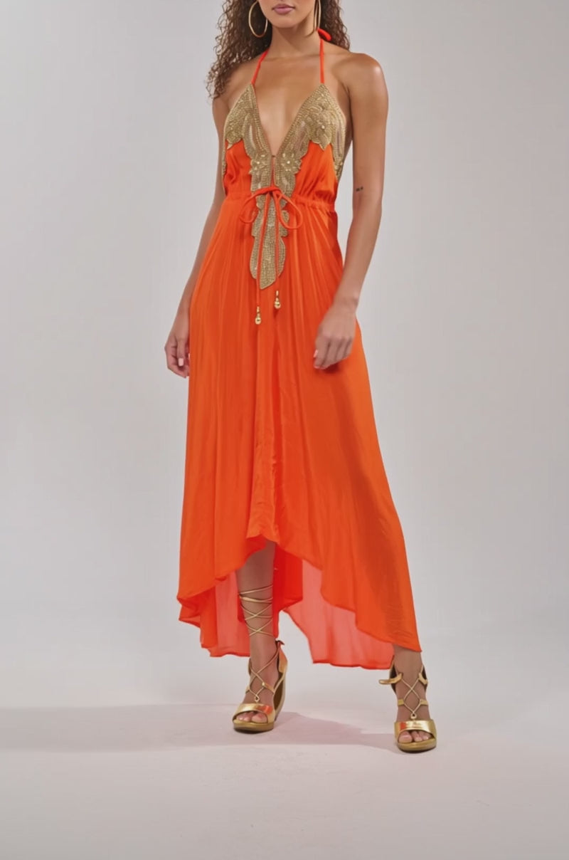 Video of woman modeling the SORRY NOT SORRY EMBELLISHED MAXI DRESS—bright orange with gold bodice embellishments—paired with gold strappy sandals against a light background, ideal for evening occasions.
