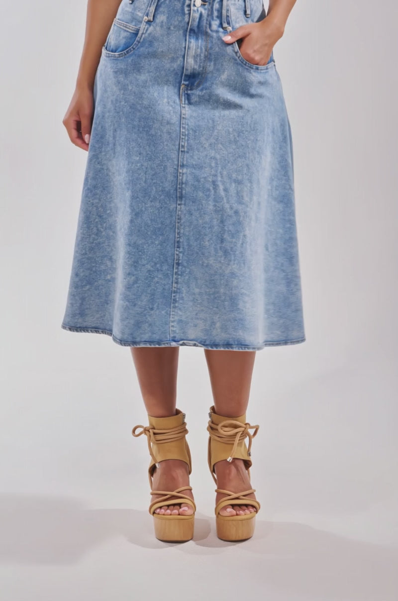 Video of woman modeling the BRITNEY MIDI DENIM SKIRT in light blue, high waisted and flared with front pockets, styled with tan platform ankle-strap sandals