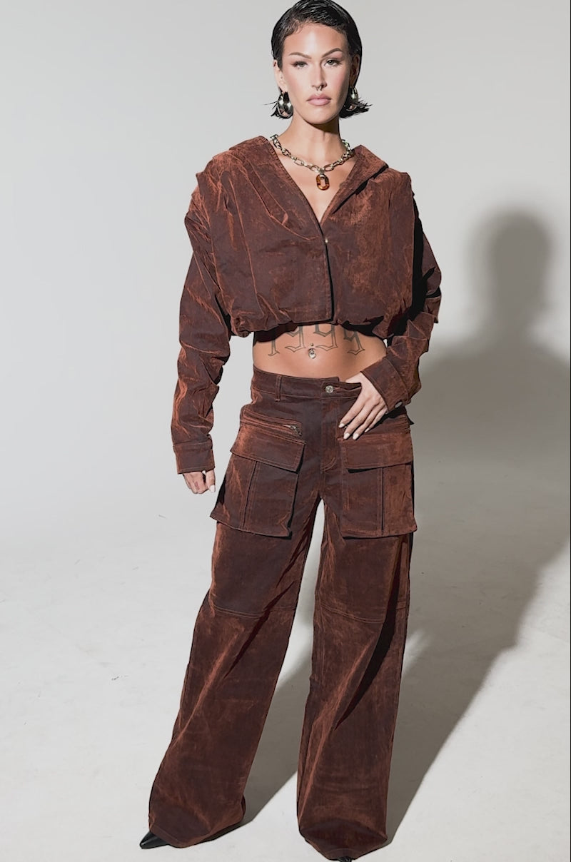 Video of woman modeling the THINK ABOUT YOU ALL THE TIME VELVET DENIM LONG SLEEVE TOP in burnt orange with sculptural folds and a suede-like texture, paired with matching pants. The background is plain light gray.