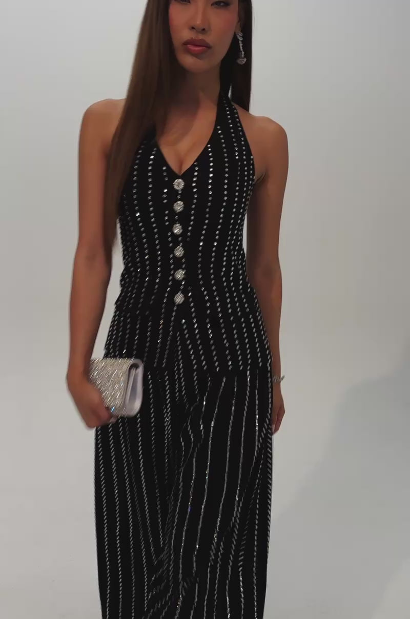 A video of a woman with long straight hair wearing the PARTY QUEEN VEST, a sleeveless black vest embellished with vertical rows of silver studs and decorative buttons. 