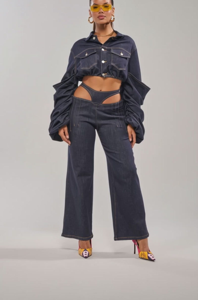 Video of woman modeling the STACKED SLEEVE CROPPED DENIM JACKET with oversized sleeves and high-waisted cutout pants, styled with gold hoop earrings, a chain necklace, and yellow-tinted sunglasses for a bold layered look.