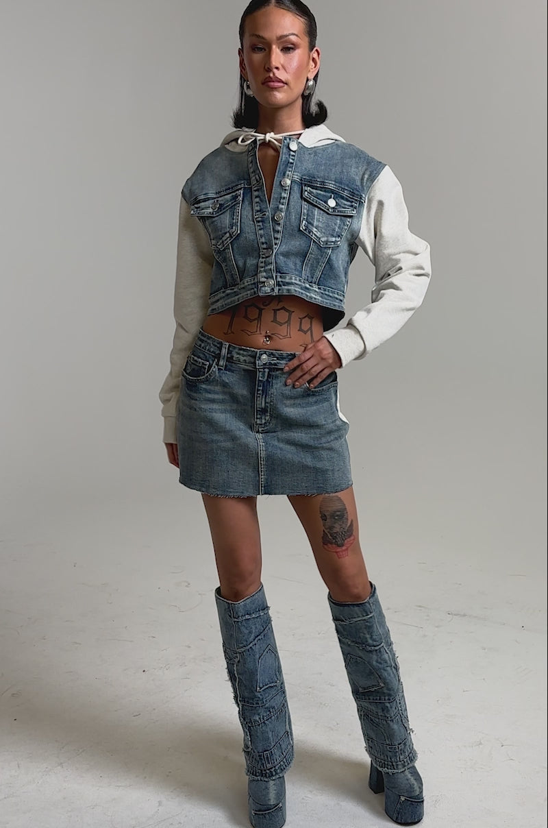 A video of a woman wearing the AFTER HOURS DENIM JACKET with beige sleeves, paired with a denim mini skirt and boots. 