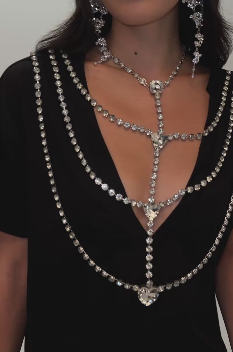 Video of a woman modeling the DIAMONDS DANCING RHINESTONE DETAIL TEE IN BLACK, styled with blue rhinestone-embellished jeans and cross motifs, a silver clutch, and statement jeweled earrings.