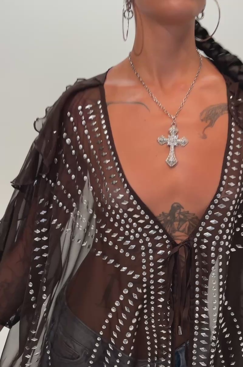 Video of a woman modeling the INDIO VIBES TIE FRONT CARDIGAN—a sheer, long brown chiffon duster adorned with silver embellishments.