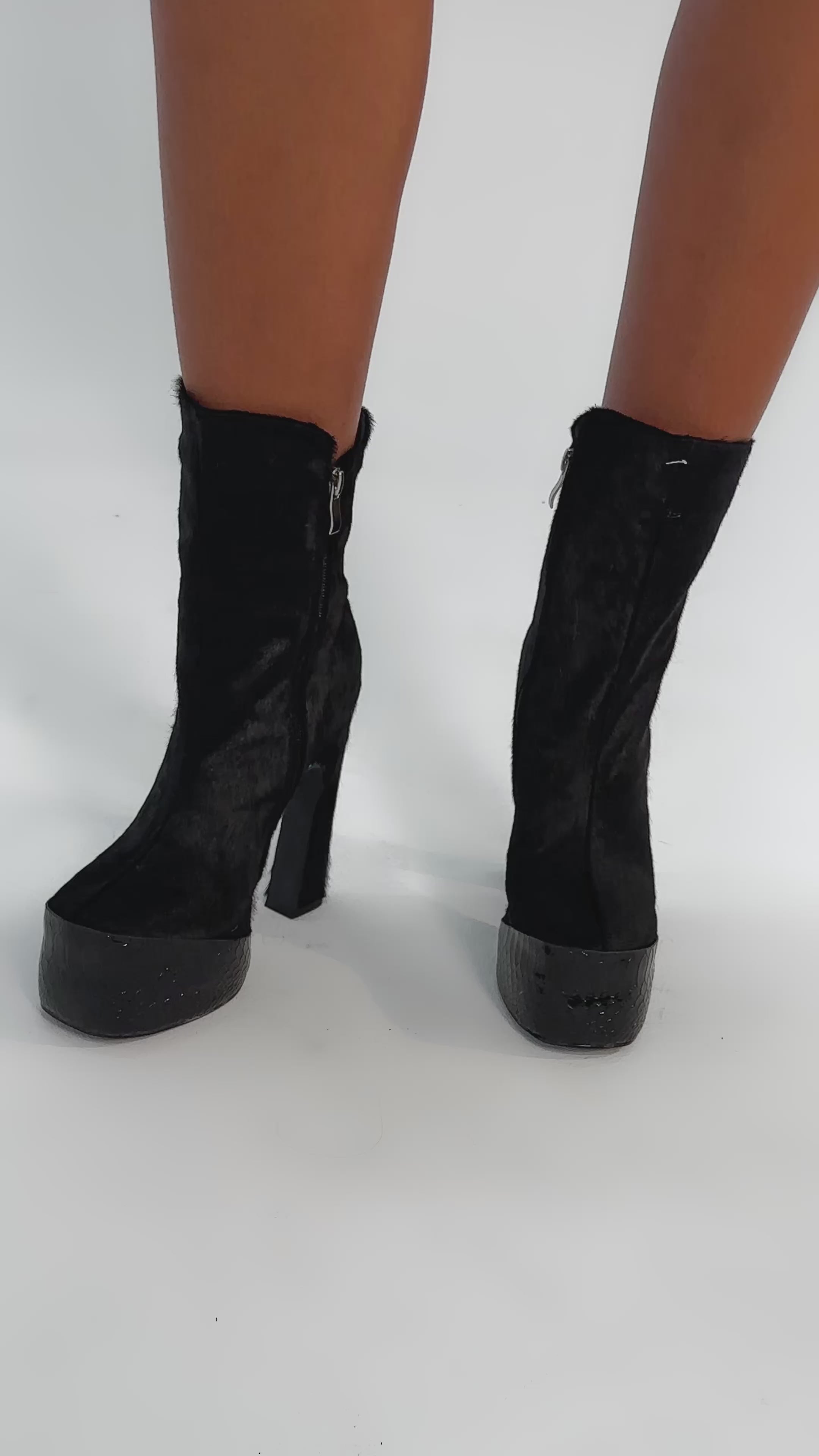 Video of woman modeling the AKIRA GOLD TROT BLACK BOOTIE—black platform heel boots with side zippers, block heels, and a textured genuine calf hair finish—set against a plain, light-colored background.