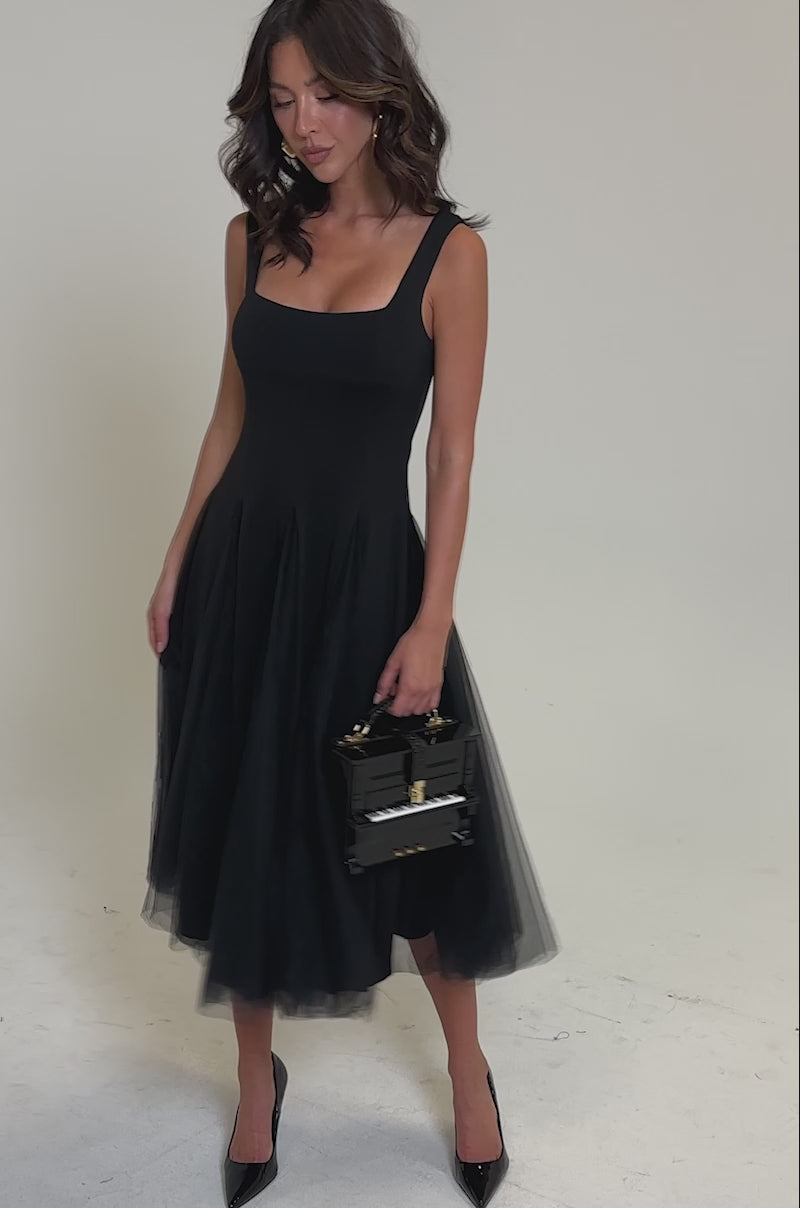 Video of woman modeling the KNOW YOUR WORTH TULLE MIDI DRESS IN BLACK—sleeveless with a layered tulle skirt—styled with black heels and a small black handbag.