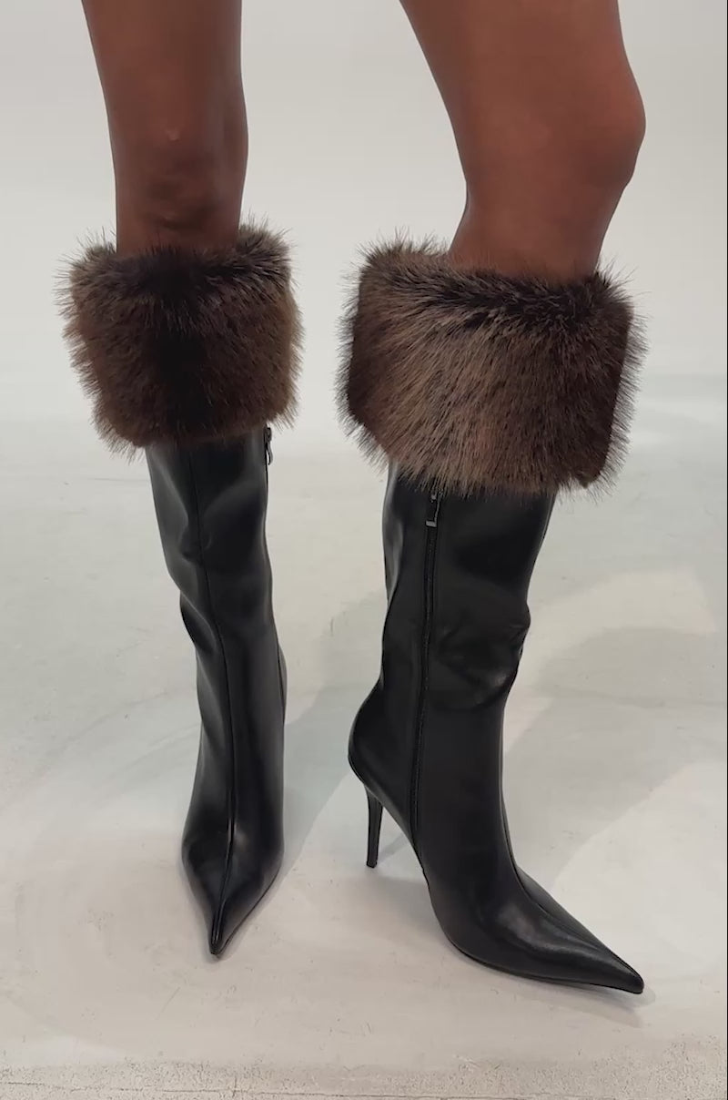 Video of woman modeling the AZALEA WANG DOVE BLACK FUR TOPLINE BOOT, a black faux leather, knee-high stiletto with a pointed toe and brown faux fur cuff, shown against a white background.