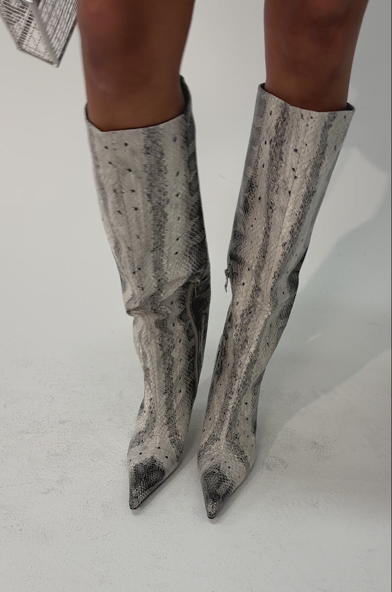 Video of woman modeling the AZALEA WANG MADEYE SNAKE STILETTO BOOT—knee-high, pointed-toe boots in a gray and black snakeskin pattern—paired stylishly with an olive green skirt.