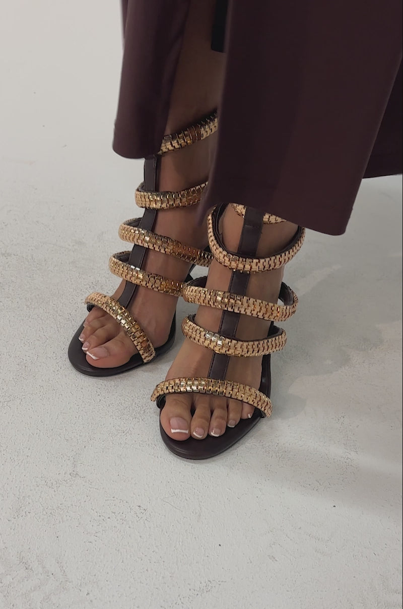 Video of woman modeling the AZALEA WANG HERSILIE BROWN GLADIATOR STILETTO heels with gold chain accents, and holding a gold textured clutch