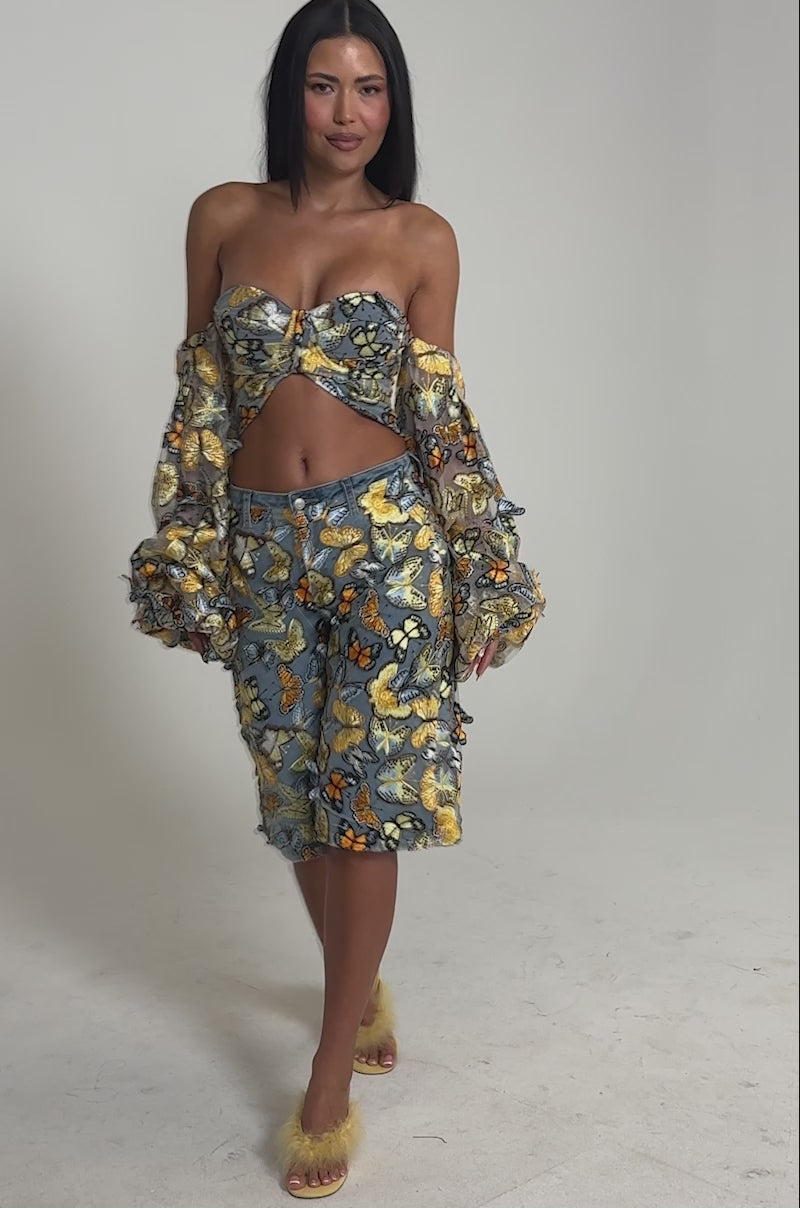 Video of woman modeling the BUTTERFLY EFFECT BERMUDA SHORT with a matching puffy-sleeve top and yellow heels