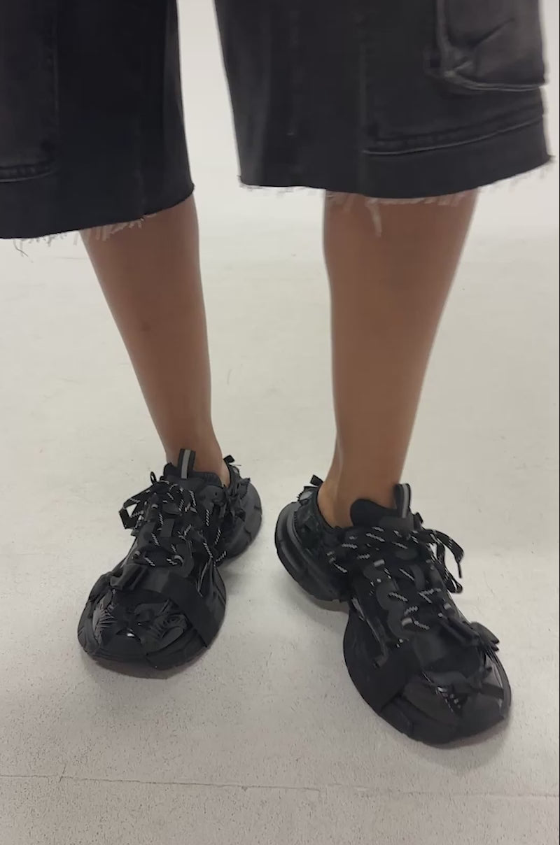 Video of woman modeling the AKIRA GOLD LOCKET BLACK SLIP ON SNEAKER featuring a black mesh and rubber design with open-heel, rugged sole, deconstructed details and bold platform edge, 