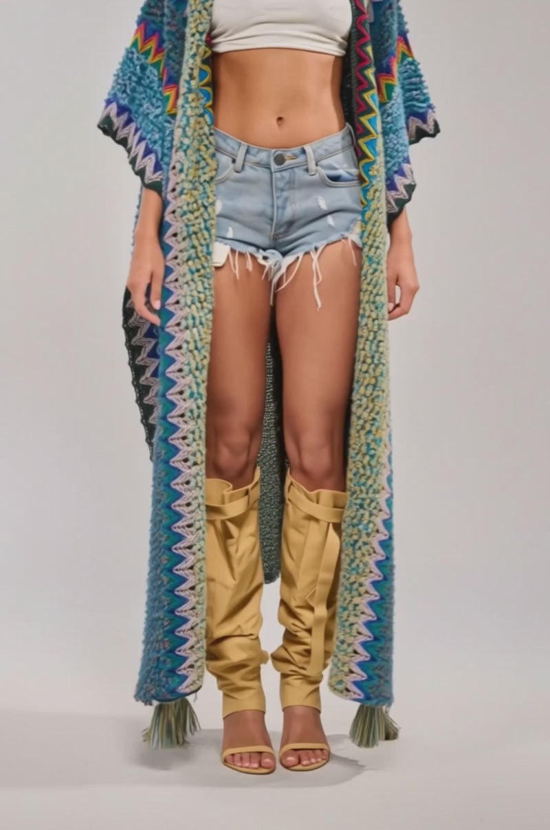Video of woman modeling the DESERT MOSAIC LONG CARDIGAN over a white crop top, distressed denim shorts, tall tan boots, and gold jewelry—perfect festival wear.