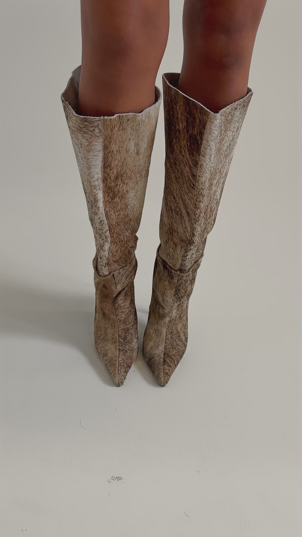 A video of a person wearing the AZALEA WANG ANSEL BROWN COW HAIR STILETTO BOOT, featuring a faux-fur animal print, standing on a light floor.