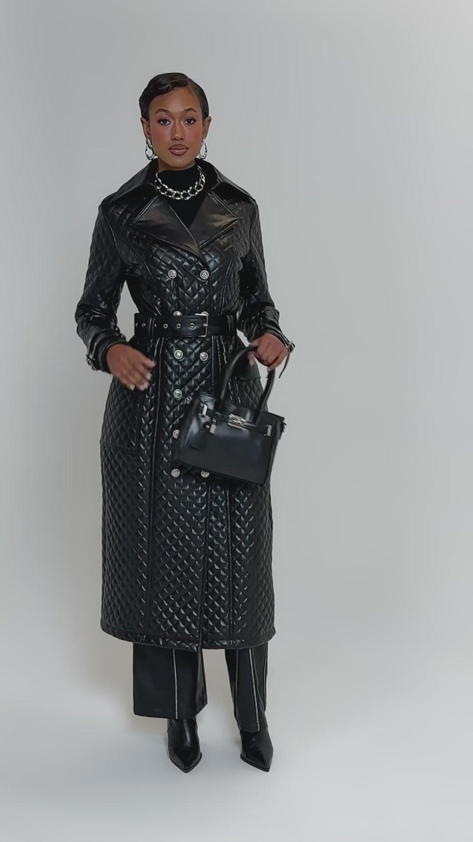 Video of woman modeling the MADISON AVE QUILTED TRENCH, styled with black wide-leg pants, pointed boots, a black handbag, earrings, and layered necklaces.