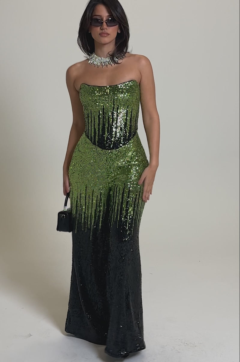A video of a woman wearing the SWEET THING SEQUIN CORSET, a strapless ombre green jumpsuit fading to black, styled with sunglasses, a chunky necklace, and a small black handbag.