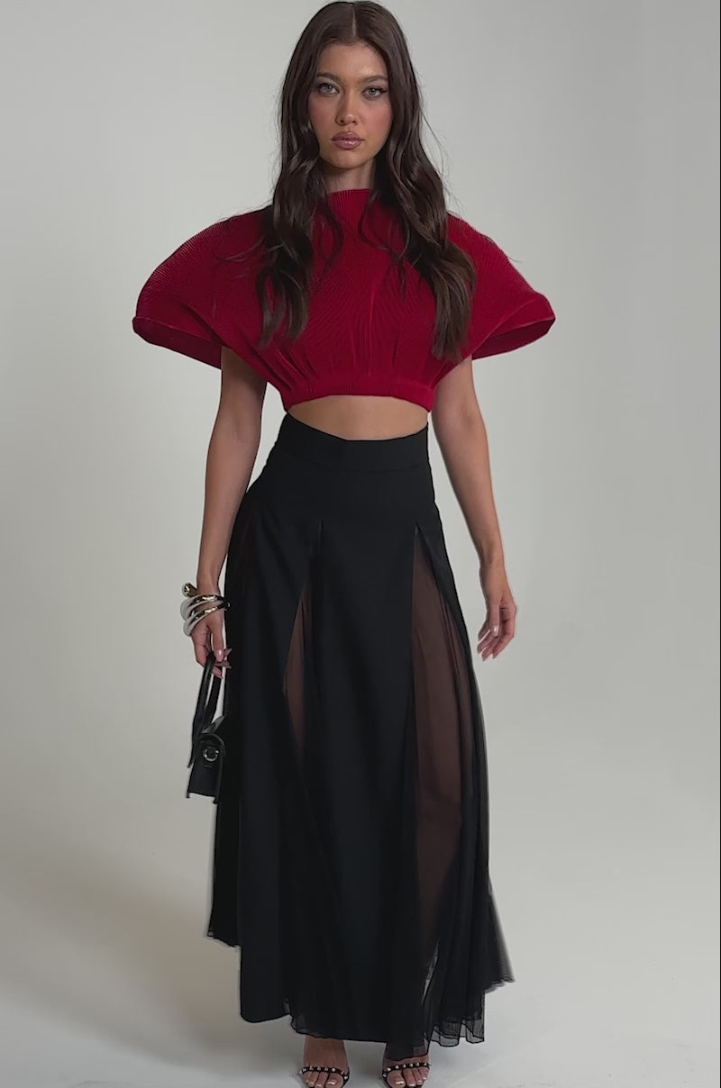 Video of woman modeling the ALL ABOUT THE DRAMA TOP, a pleated red crop top with batwing sleeves, paired with a high-waisted black skirt featuring sheer panels. 