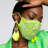 A person is wearing the READY WHEN YOU ARE RHINESTONE FASHION FACE COVER, accentuated with a beaded net pattern. They have also accessorized with neon green tassel earrings. With their hand partially raised to display black nail polish, they complete the look with a vibrant green outfit, achieving a bold and fashionable appearance.