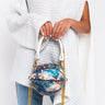 A person wearing a white, knitted poncho and blue jeans is holding the stylish RENAISSANCE MINI TOP HANDLE BASKETBALL BAG, featuring a round design with a blue and gold floral pattern. The bag has white handles adorned with gold chain details. The person is partially visible from the shoulders down.