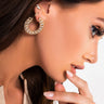 A close-up of a person with long brown hair, adorned with the RICH BITCH RHINESTONE EARRING by Simpo Import&Export Co., Ltd. They also wear a smaller stud earring in the same ear. The person touches their mouth with manicured nails and wears a satin-like garment against a plain white background.